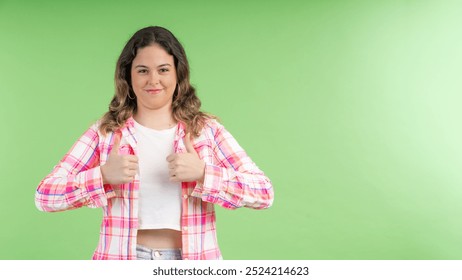 Young woman is smiling and showing a thumbs up gesture with both hands against a green screen background - Powered by Shutterstock