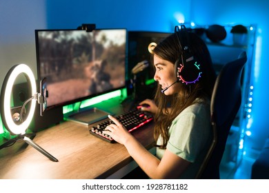 Young Woman Smiling And Talking During A Live Stream On A Smartphone With A Ring Light. Happy Female Gamer Playing A Video Game In Her Computer With Neon Led Lights