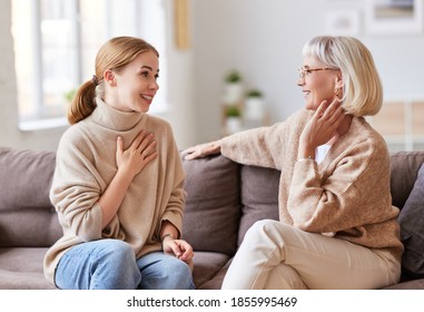 Young woman smiling and talking with senior mother while sitting on comfortable sofa at home together
