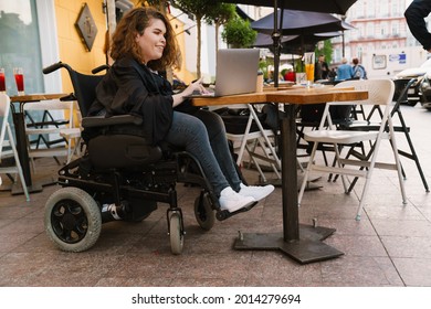 Young woman smiling and using laptop while sitting in wheelchair at cafe outdoors