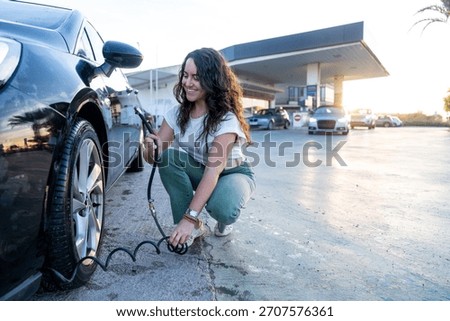 Young woman smiling while checking car tire pressure at a service station