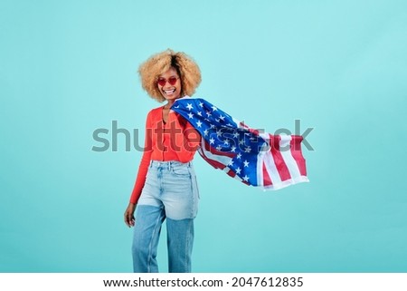Young woman smiling while holding a US flag on an isolated background.