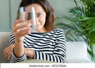 Young Woman Smiling While Looking At The Camera Through The Glass Of Water. Health Benefits Of Drinking Enough Water Concepts. 