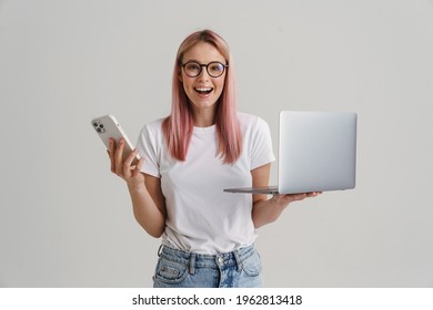 Young woman smiling while posing with laptop and cellphone isolated over white background