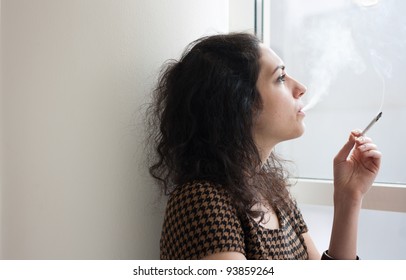 Young Woman Smoking Indoors At A Window (portrait With Copy Space)