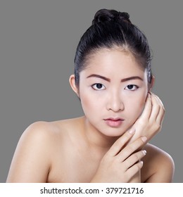 Young woman with smooth skin and beautiful face, looking at camera against grey background