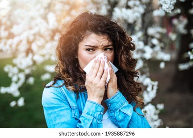 Young woman sneezing in park. Allergy, flu, virus concept.
