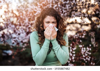 Young woman sneezing in park. Allergy, flu, virus concept.