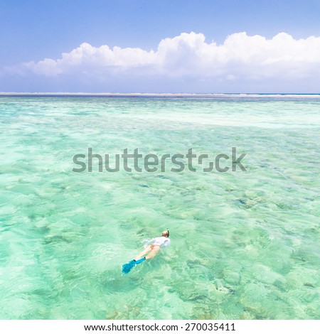 Young woman snorkeling in clear shallow sea of tropical lagoon with turquoise blue water and coral reef,  near exotic island. Mnemba island, Zanzibar, Tanzania.