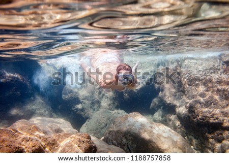 Young woman snorkeling near rocks underwater in the tropical sea