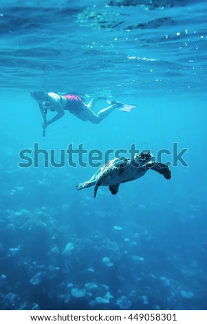 young woman snorkeling with selfie stick and action camera take photo turtle