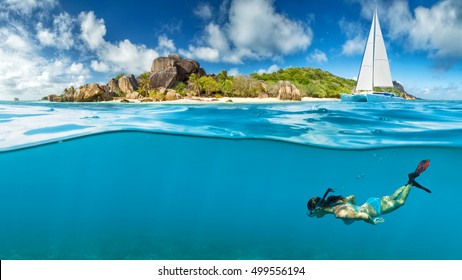 Young woman snorkling next to tropical island. Anchoring catamaran on background