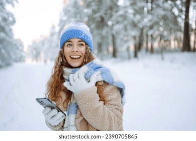 A young woman in a snowy park with a phone in her hands communicates via video and takes a selfie. Beautiful female tourist with phone having fun outdoors. Travel concept. - Powered by Shutterstock