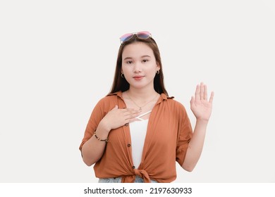 A young woman solemnly swears she is not lying. Putting her hand on her chest and raising her hand to make a vow. Making an oath. Isolated on a white background. - Shutterstock ID 2197630933