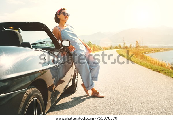 Young woman solo traveler stay near cabriolet car on\
picturesque mountain road