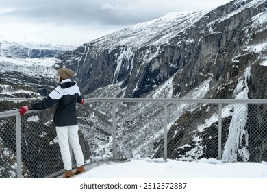 A young woman solo traveller looks out over a frozen Voringfossen waterfall in Norway in the depth of winter. - Powered by Shutterstock