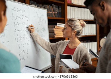 Young woman solving mathematics problem on whiteboard. College student solving algebra equation on white board in library with students. Girl trying to understand mathematics problem during lesson.