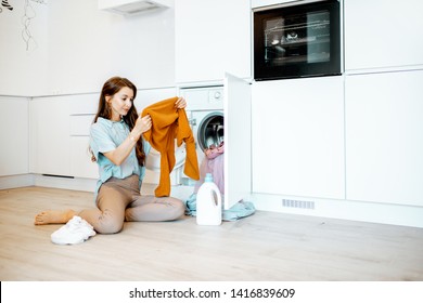 Young Woman Sorting Dirty Clothes While Sitting On The Floor Near The Washing Machine At Home