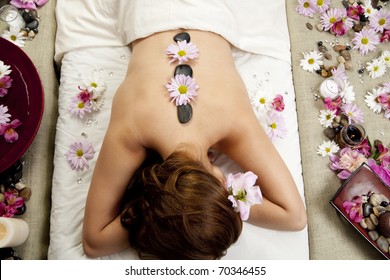 A Young Woman At A Spa Waiting For A Massage With Hot Stones And Flowers On Her Back.