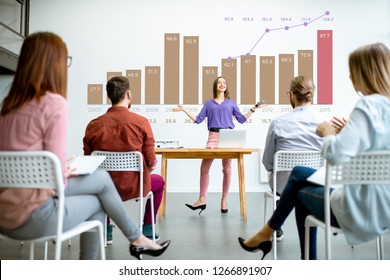 Young Woman Speaker Reporting To The Audience During The Meeting In The Conference Room With Charts On The Background