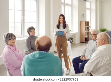 Young woman speaking on meeting in nursing home in front of small group of senior people about dementia prevention. Elderly men and women sitting on chairs in circle and listening speaker on seminar. - Powered by Shutterstock