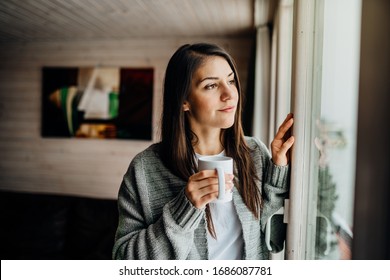 Young woman spending free time home.Self care,staying home.Enjoying view,gazing through to the window.Quarantined person indoors.Serene mornings.Avoiding social contact. - Shutterstock ID 1686087781