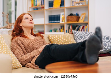 Young Woman Spending Quality Time Relaxing At Home With Her Feet Up Lookig Into The Air With A Dreamy Expression In A Low Angle View