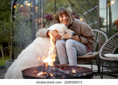 Young woman spends evening time with her cute white dog, sitting by the fire in garden at cozy and beautiful atmosphere - Powered by Shutterstock