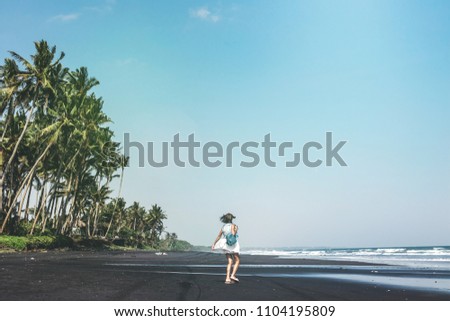 Young woman is spinning on a black sand beach, Bali island.