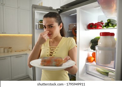 Young Woman With Spoiled Sausage Near Open Refrigerator In Kitchen