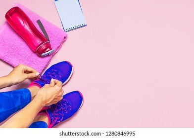 Young woman in sporting blue leggings laces sneakers, preparing for training. Accessories for sports, bottle of water towel notebook on pastel pink background flat lay top view. Fitness concept - Shutterstock ID 1280846995