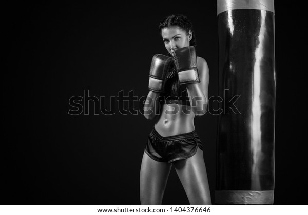 Young woman\
sportsman boxer doing boxing training at the gym. Girl wearing\
gloves, sportswear and hitting the punching bag. Isolated on black\
background with smoke. Copy\
Space.