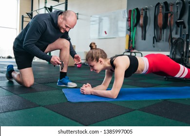 Young woman in sportswear doing exercise plank with male Instructor notes time on a stopwatch. Endurance exercise in the gym - Shutterstock ID 1385997005