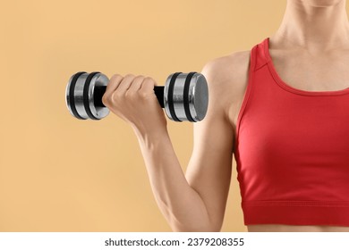 Young woman in sportswear doing exercises with dumbbells on beige background, closeup. Space for text