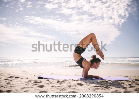 Young woman in sportswear doing yoga asana on the beach. Fitness female practicing pincha mayurasana scorpion along the sea.
