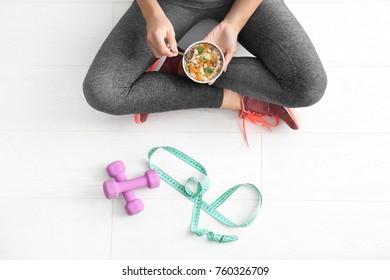 Young Woman In Sportswear Eating Oatmeal On Floor