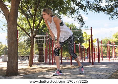 Young woman in sportswear having knee problems on sports ground