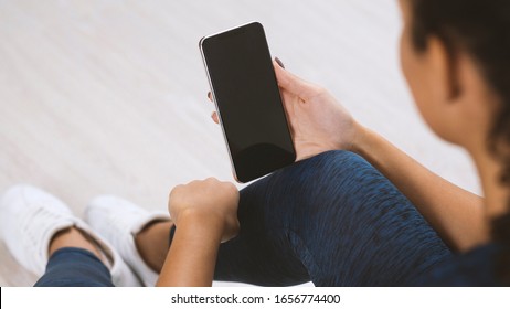 Young Woman In Sportswear Holding Mobile Phone With Blank Screen Indoors, Closeup View. Mockup For Design