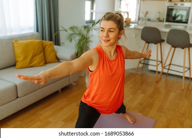 Young Woman In Sportswear Making Warrior Yoga Exercise At Home. Young Woman Exercising At Home Due To COVID 19 Pandemic.