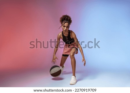 Young woman in sportswear playing basketball on studio background with color filter