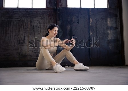 young woman in sportswear sits on the floor and drinks from a bottle in her hand and relaxes after workout in the gym, trainer cooldown with water after exercise