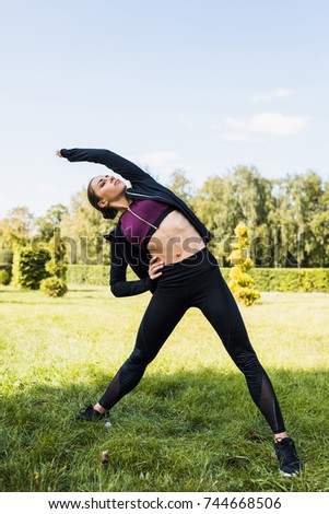 young woman in sportswear stretching in park
