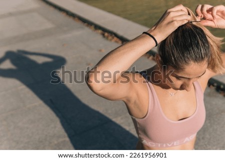 Young woman in sporty tight top putting her hair up or making a ponytail to start playing sports outdoors.