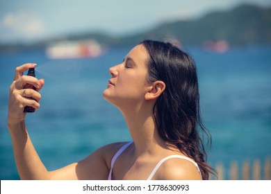 Young Woman Spraying Thermal Water Or Facial Mist On Her Face At The Beach. Summer Skin Care