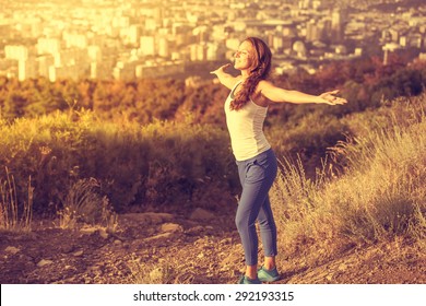 Young Woman Spreading Hands Wide Open With City On Background. Freedom Concept. Love And Emotions, Woman Happiness. Toned Image