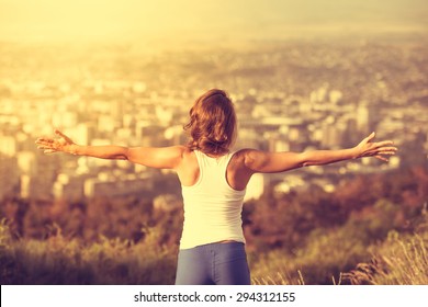 Young woman spreading hands wide open with city on background. Freedom concept. Love and emotions, woman happiness. Toned image