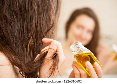 Young Woman Spreading Oil Mask Over Her Hair In Front Of A Mirror