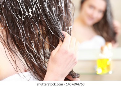 Young woman spreading oil mask over her hair in front of a mirror