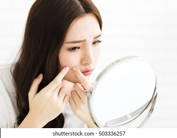 young woman squeeze her acne in front of the mirror