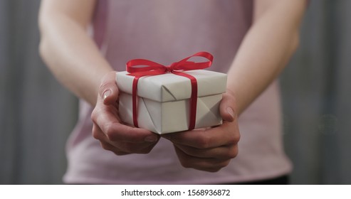 young woman stand and show white gift box with red ribbon bow